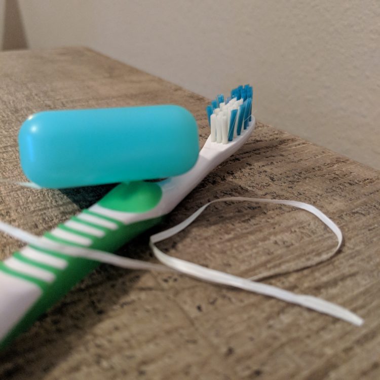 Toothbrush with white and green accents and a small plastic case of dental floss resting next to it